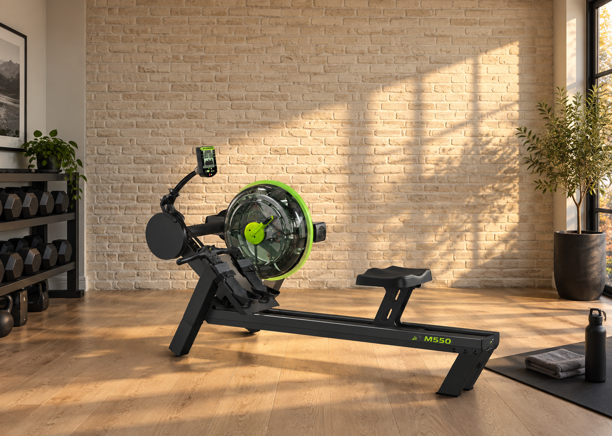 Dynamic Fluid M550 water rower in a brick-wall training studio with a dumbbell rack