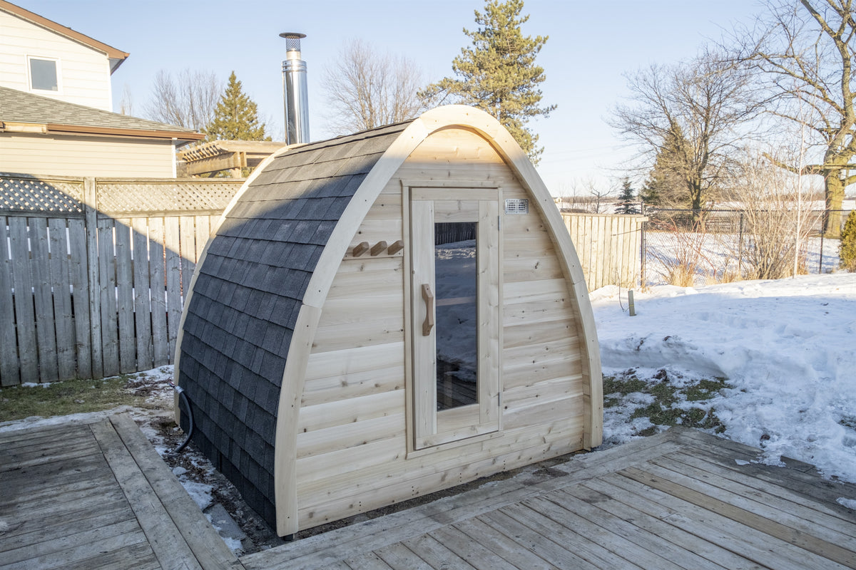 MiniPOD Sauna installed on a timber deck, three-quarter view showing the shingled flank and glass door